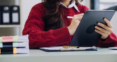 Young business woman sitting in office at table and using smartphone. On desk is laptop and tablet computer, on screen charts and graphs. Woman analyzing data. Student learning online. photo