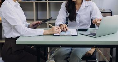 Young business woman sitting in office at table and using smartphone. On desk is laptop and tablet computer, on screen charts and graphs. Woman analyzing data. Student learning online. photo