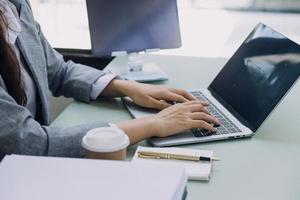 Young business woman sitting in office at table and using smartphone. On desk is laptop and tablet computer, on screen charts and graphs. Woman analyzing data. Student learning online. photo