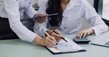 Young business woman sitting in office at table and using smartphone. On desk is laptop and tablet computer, on screen charts and graphs. Woman analyzing data. Student learning online. photo