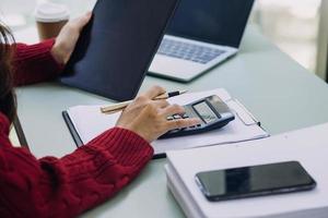 Young business woman sitting in office at table and using smartphone. On desk is laptop and tablet computer, on screen charts and graphs. Woman analyzing data. Student learning online. photo