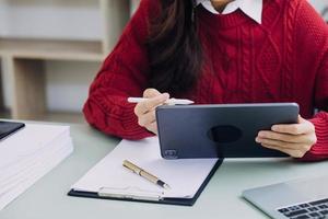 Young business woman sitting in office at table and using smartphone. On desk is laptop and tablet computer, on screen charts and graphs. Woman analyzing data. Student learning online. photo