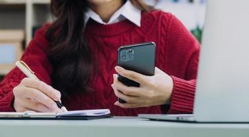 mujer de negocios joven sentada en la oficina en la mesa y usando un teléfono inteligente. en el escritorio hay una computadora portátil y una tableta, en gráficos y gráficos en pantalla. mujer analizando datos. estudiante aprendiendo en línea. foto