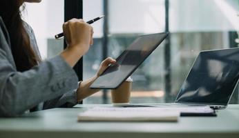 Young business woman sitting in office at table and using smartphone. On desk is laptop and tablet computer, on screen charts and graphs. Woman analyzing data. Student learning online. photo