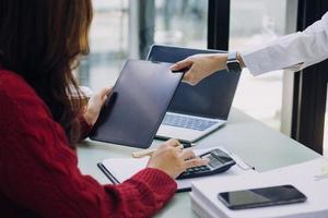 Young business woman sitting in office at table and using smartphone. On desk is laptop and tablet computer, on screen charts and graphs. Woman analyzing data. Student learning online. photo