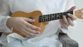 Close-up shot of white casual shirt musician playing wooden acoustic Ukulele, stringed musical instrument by fingers, relaxing by singing a classic song melody sound, performing skill in note chords. video