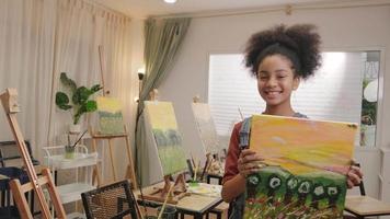 One Black student girl shows her painting work, proud with portfolio, acrylic color picture on canvas in art classroom and creative learning with talents skill at elementary school studio education.