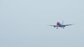 photo frontale de l'atterrissage d'un avion rouge moderne, avec des trains d'atterrissage vus libérés. le ciel bleu est tout autour de l'avion. l'avion de ligne descend en douceur en s'approchant video