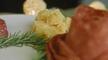 assiette de charcuterie avec salami, différentes sortes de fromages. il contient des fruits secs, diverses noix et du miel. arrangement de vacances avec des bougies allumées video