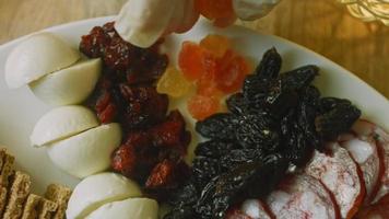 prato de charcutaria com salame, diferentes tipos de queijo. tem frutas secas, nozes diversas e mel. arranjo de férias com velas acesas video