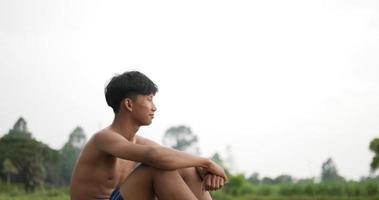Back view of young farmer without shirt sitting on the ground and looking over his rice fields, He smile with proud after plants video