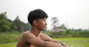 side view and close up young farmer without shirt sitting on the ground and looking over his rice fields, He smile with proud after plants video