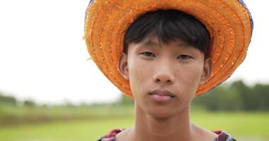 cámara lenta, retrato en la cabeza de un granjero, retrato de un adulto joven con camisa a cuadros y sombrero de pie y mira el campo de arroz de la cámara en el fondo video