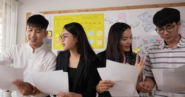 avvicinamento di quattro attività commerciale persone avendo un discussione mentre in piedi nel un ufficio. asiatico uomo e donna Tenere documento. opera colleghi discutere nel posto di lavoro. avendo conflitto combattimento a posto di lavoro concetto. video