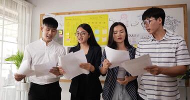 Vier Geschäftsleute haben einen Streit, während sie in einem Büro stehen. asiatischer mann und frau, die dokument halten. arbeitskollegen streiten am arbeitsplatz. Konfliktkampf am Arbeitsplatzkonzept haben. video