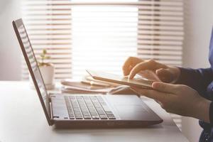 Businessman or accountant typing keyboard on laptop computer with business documents on office table with blurred window background. concept of document work Connecting internet network technology photo