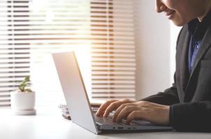 Businessman or accountant typing keyboard on laptop computer with business documents on office table with blurred window background. concept of document work Connecting internet network technology photo
