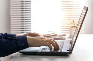 Businessman or accountant typing keyboard on laptop computer with business documents on office table with blurred window background. concept of document work Connecting internet network technology photo