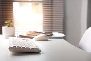 Side view of white keyboard on desk with blur light illuminating window in office. office workspace, freelance office corner photo