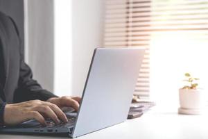 Businessman or accountant typing keyboard on laptop computer with business documents on office table with blurred window background. concept of document work Connecting internet network technology photo