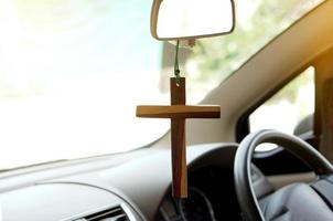 Closeup wooden crucifix hang  in  front steering wheel and console of the car. Concept, talisman,amulet to prevent accidents. Belief, faith,holy  in god to protect when driving. photo