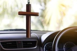 Closeup wooden crucifix hang  in  front steering wheel and console of the car. Concept, talisman,amulet to prevent accidents. Belief, faith,holy  in god to protect when driving. photo