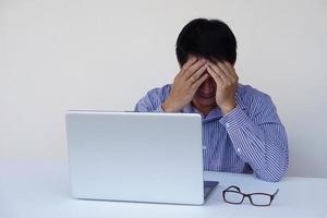 Asian man officer feel depressed during working on computer laptop, covered  face with hands. Concept, hard working, using idea for work, think too much, headache, stressed. photo