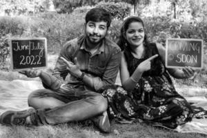 pareja india posando para una sesión de fotos de maternidad. la pareja está posando en un césped con hierba verde y la mujer está faluntando su panza en el jardín de lodhi en nueva delhi, india - blanco y negro