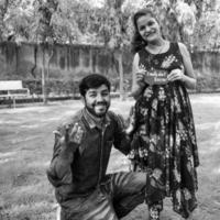 Indian couple posing for maternity baby shoot. The couple is posing in a lawn with green grass and the woman is falunting her baby bump in Lodhi Garden in New Delhi, India - Black and White photo