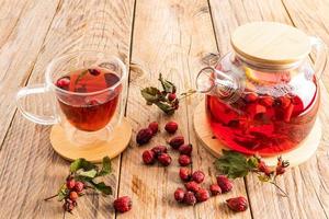 glass teapot with a decoction of freshly prepared tea with rose hips on a wooden table. vitamin useful tea for colds. photo