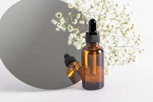 cosmetic bottle with a dropper on the background of a mirror and gypsophila. serum, essence, oil for facial skin care. natural organic cosmetics. photo