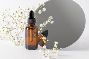 a glass bottle with a pipette against the a round mirror and gypsophila. dry skin care product. serum to moisturize the skin. brand layout. photo