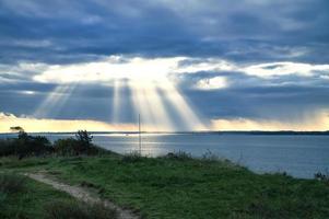 en la costa de hundested. los rayos del sol atraviesan el cielo dramático a través de las nubes foto