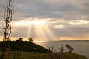 en la costa de hundested. los rayos del sol atraviesan el cielo dramático a través de las nubes foto