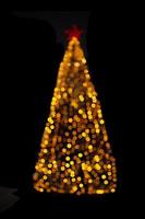 Blurred yellow Christmas tree lights on black isolated background. Design element. Defocused spruce with star. Overlay. New Year photo