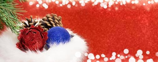 Christmas balls with cones in fur gift bag with fir branch on red blurred background with white bokeh. Banner, concept of shopping, sales. New Year. Copy space photo