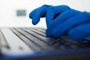 Hand in protective gloves typing on the laptop keyboard photo