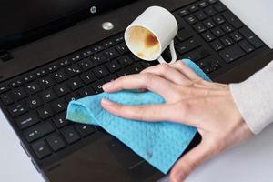 Hand cleans spilled coffee on laptop keyboard with a rag photo