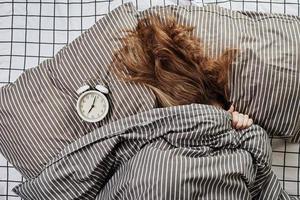 Sleeping woman covered under blanket in bed and vintage alarm clock on pillow photo