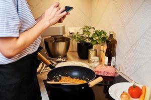 mujer cocinando salsa boloñesa y usando smartphone foto