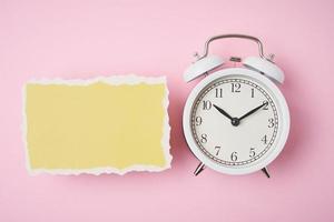 despertador blanco y hoja de papel rota vacía sobre un fondo rosa foto