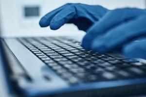 Hand in protective gloves typing on the laptop keyboard photo