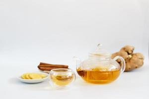 a cup of tea with ginger root, lime, cinnamon and teapot on white background. Health drink concept. photo