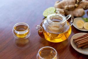 a cup of tea with ginger root, lime, cinnamon and teapot on wooden background. Health drink concept. photo