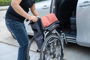 Asian woman folding and lift up wheelchair into her car. Accessibility concept. photo