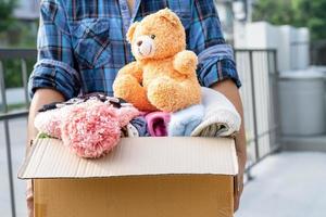 Holding clothing donation box with used clothes and doll at home to support help for poor people in the world. photo