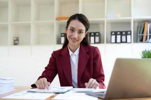 mujer de negocios asiática que usa calculadora y computadora portátil para hacer finanzas matemáticas en un escritorio de oficina, impuestos, informes, contabilidad, estadísticas y concepto de investigación analítica foto