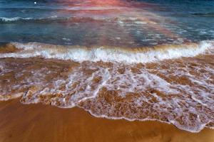 The lapping of the waves on the sandy beach.Small sea waves with crystal clear water on the sandy beach. photo