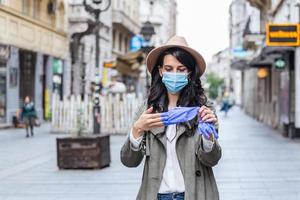 retrato de una mujer joven en la calle usando una máscara protectora para prevenir el coronavirus y el anti-smog y usando un teléfono inteligente quitándose los guantes foto