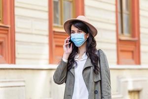 Portrait of young woman on the street wearing face protective mask to prevent Coronavirus and anti-smog and using smartphone photo